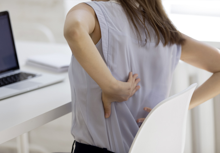 Frau mit Rückenbeschwerden im Sitzen